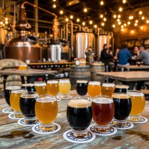 A rustic brewery setting with a variety of craft beers in tasting glasses, wooden tables with brewing equipment in the background